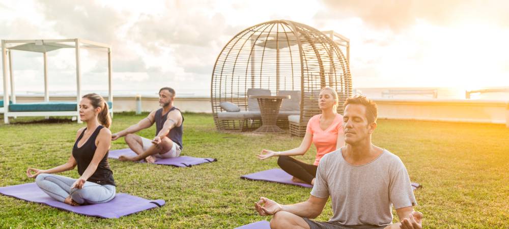 Four people sitting on a yoga mat on the grass in a yoga pose.