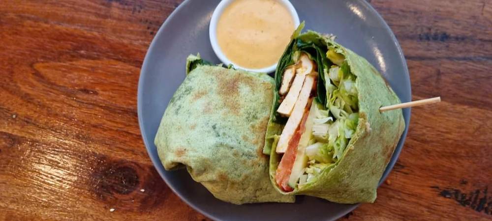 A tofu salad wrap is cut open on a plate with a side of sauce.